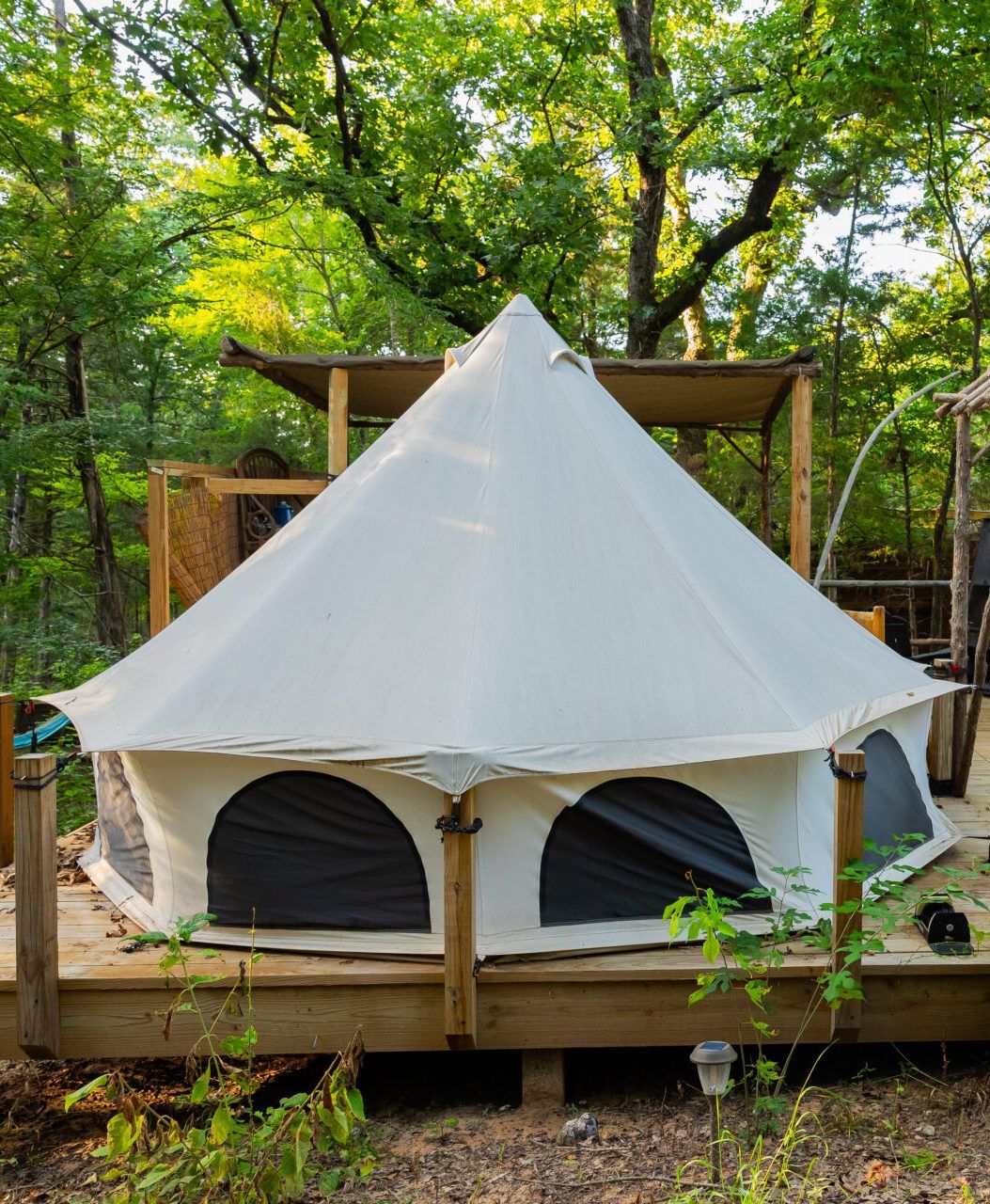 White canvas bell tent on a wooden deck in a wooded campsite