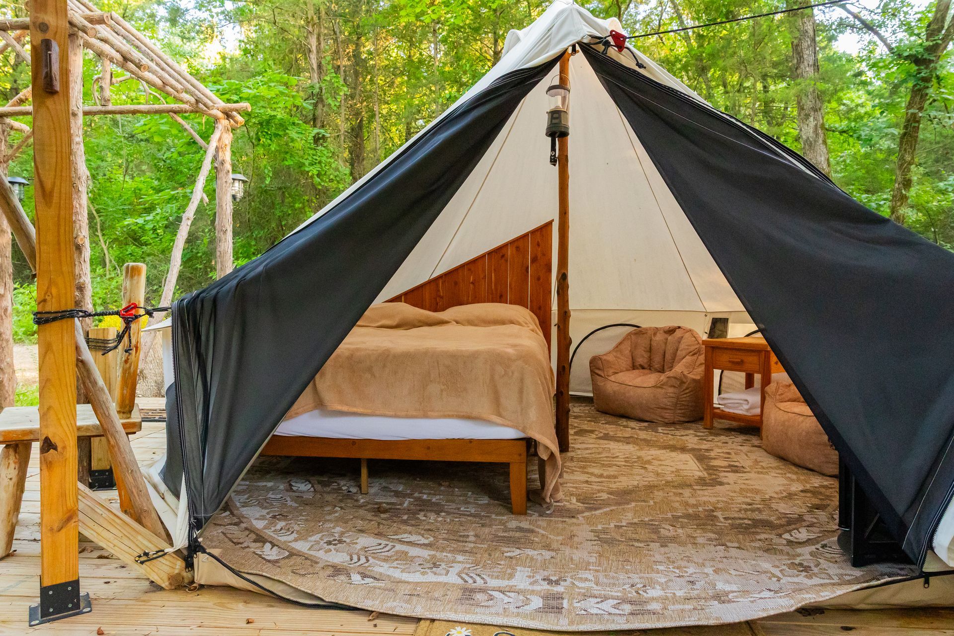 Canvas tent with a bed and seating on a circular rug in a wooded campsite