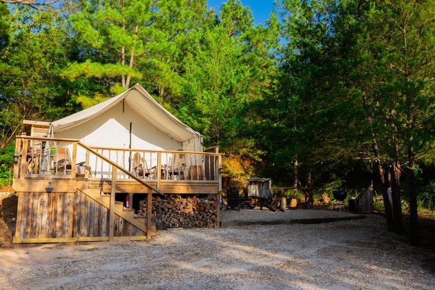 Canvas glamping tent on a wooden deck in a sunny wooded campsite