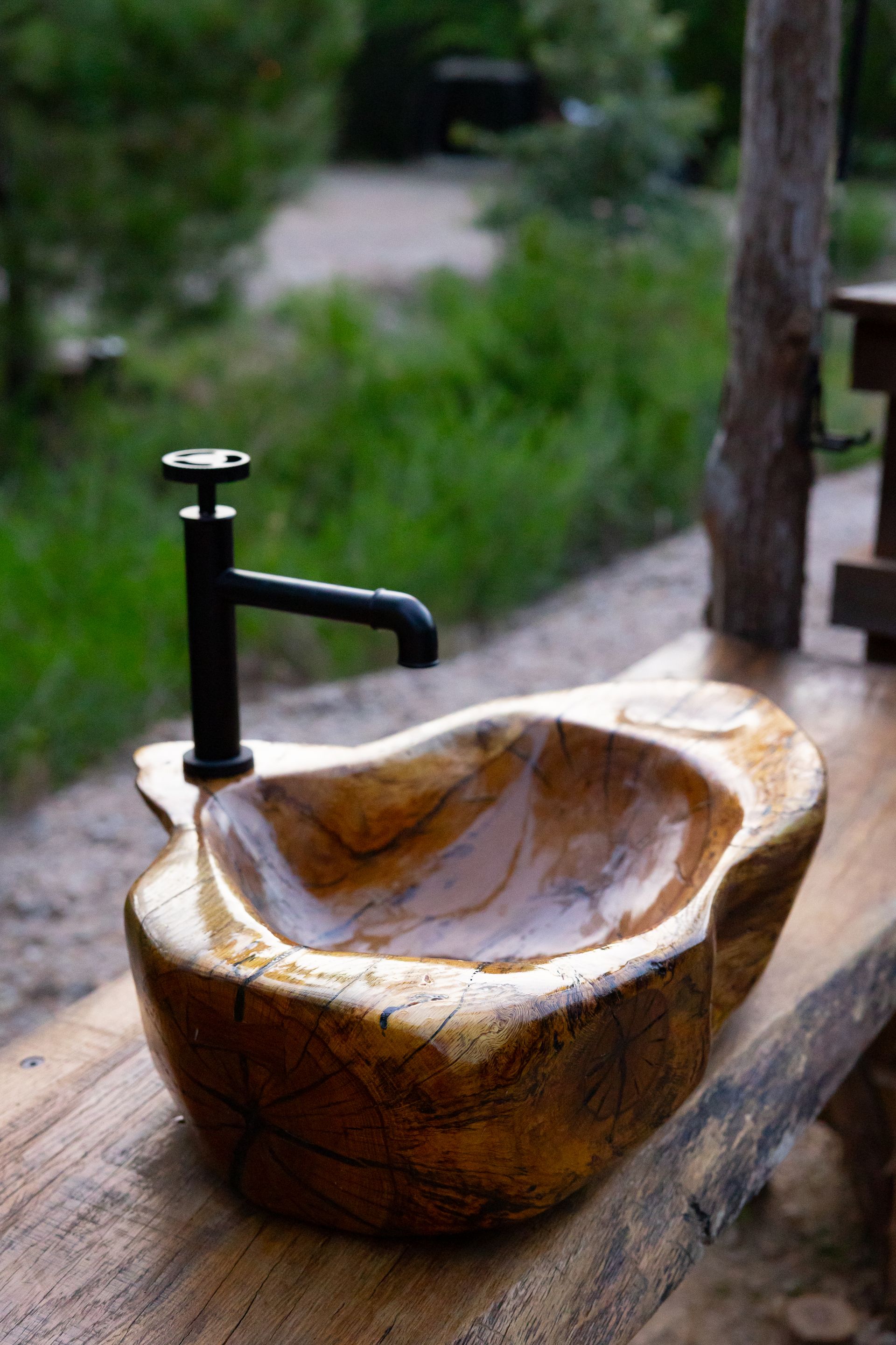 Stone sink with black faucet on a wooden counter outdoors