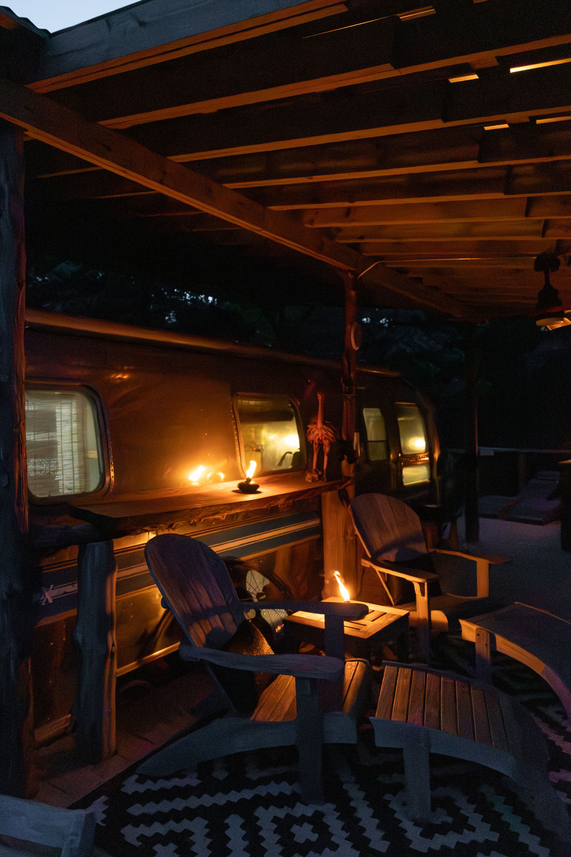 Cozy candlelit porch with wicker chairs, a small table, and windows glowing in the dark outside.
