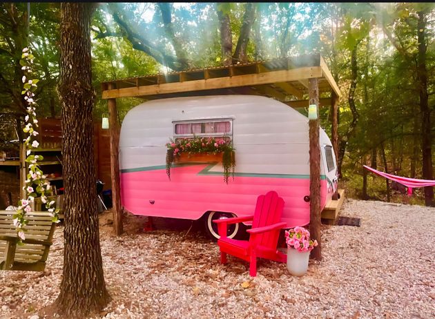 Pink and white camper in a wooded campsite with red chairs and gravel ground