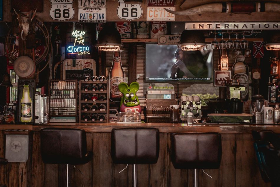 Rustic bar interior with wooden stools, shelves of bottles, and vintage Route 66 signs