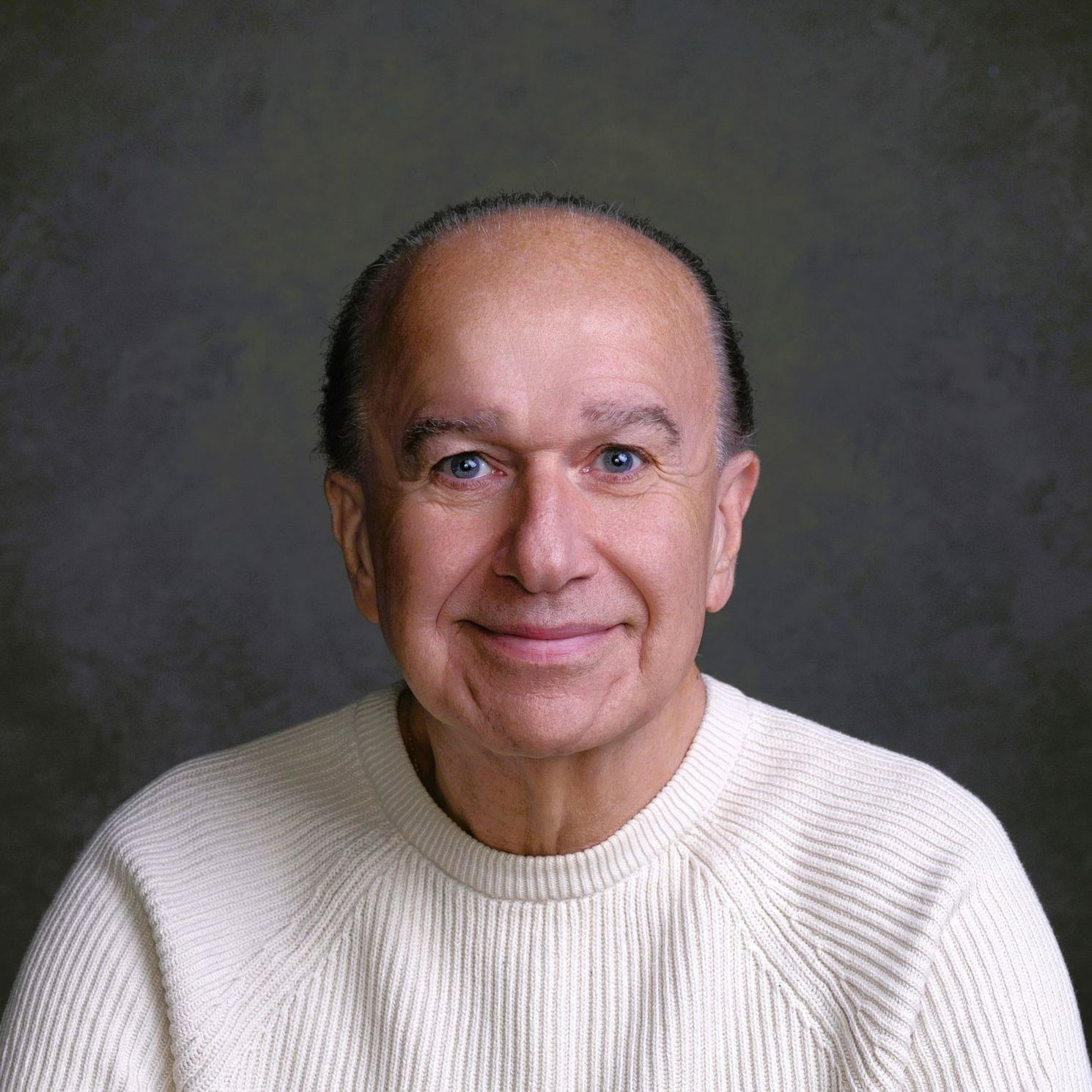 A man wearing a white sweater is smiling for the camera.