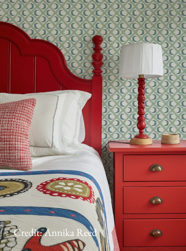 Annika Reed design bedroom with red furniture, crescent moon patter on wallpaper and contrasting larger-scale patterns on bed linen.
