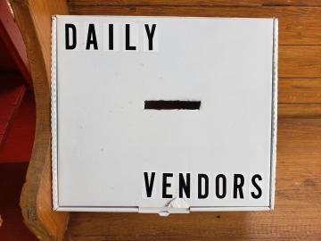 White sign reading “DAILY” and “VENDORS” with a short black dash in the center.
