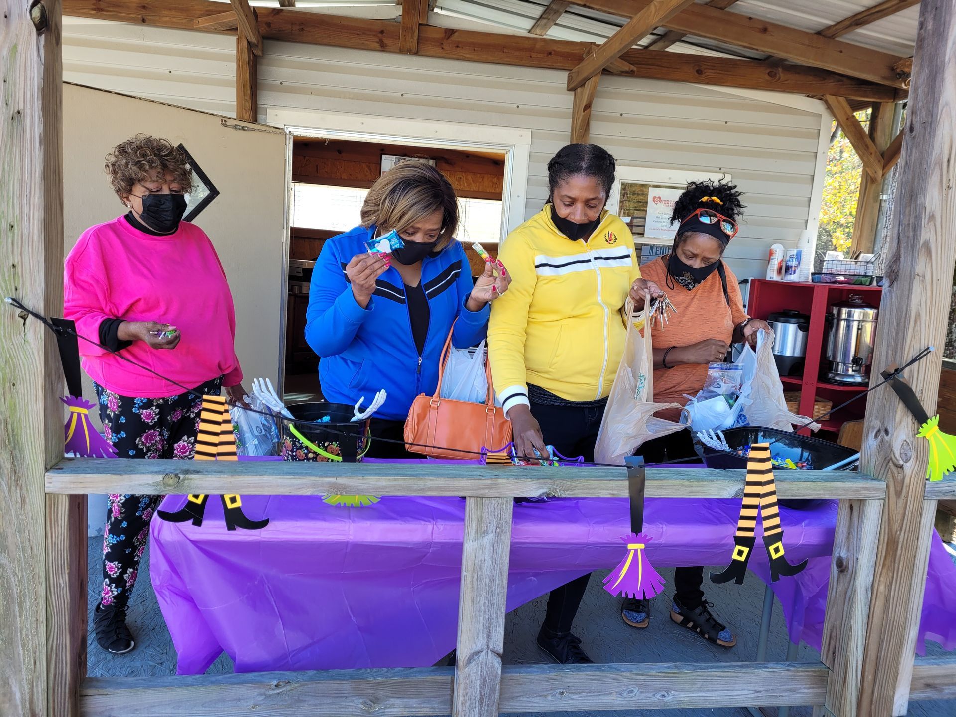 People browsing small items at a purple-covered craft table in a wooden pavilion