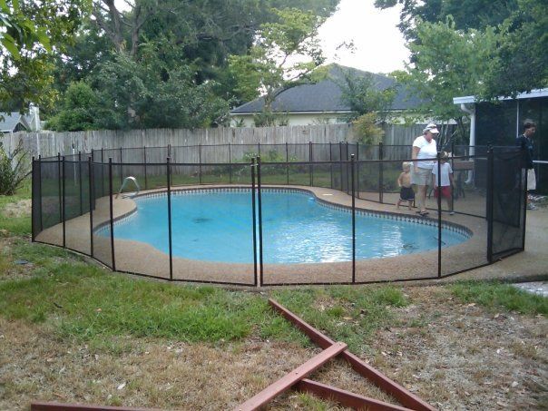 A fence surrounds a swimming pool in a backyard