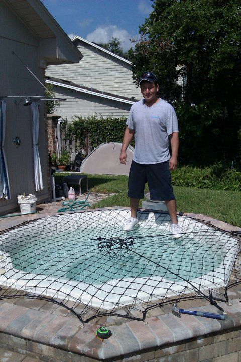 A man is standing on top of a hot tub covered in a net.