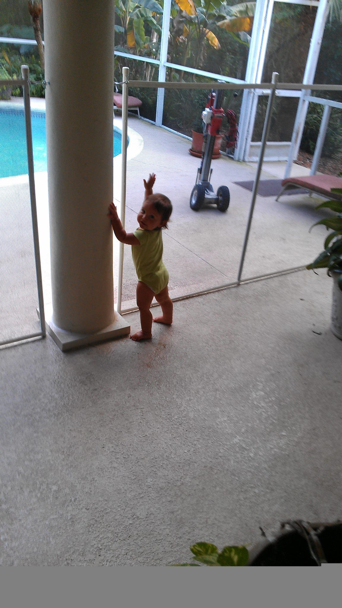 A little girl is standing next to a fence in front of a pool.