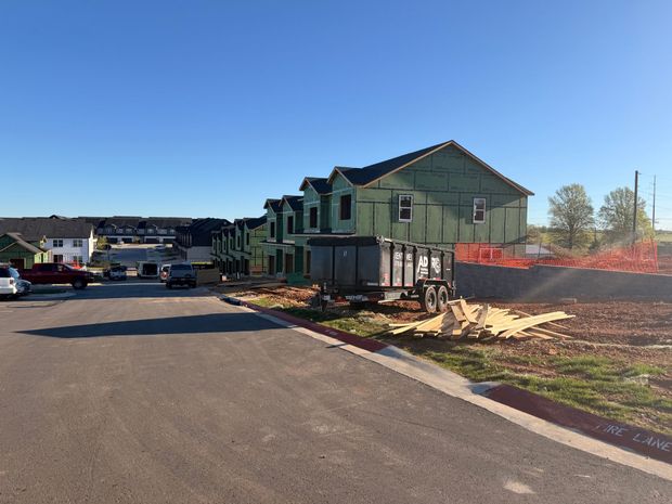 A residential construction site with several wooden frame houses and a trailer under a clear blue sky.