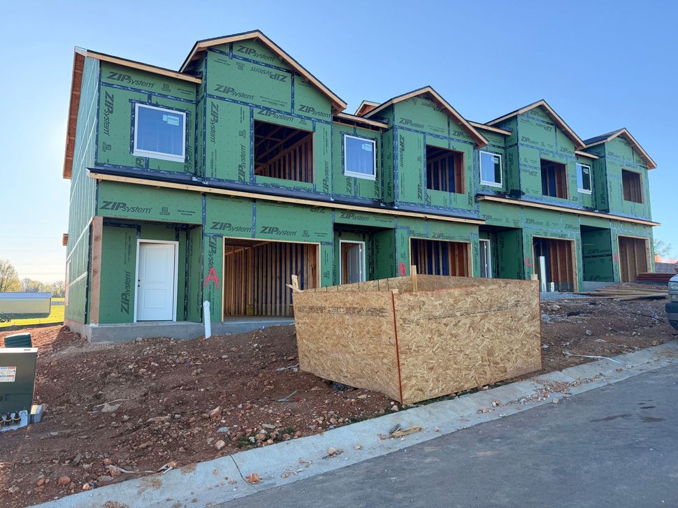 A multi-unit townhouse construction site with green wall sheathing, exposed wooden frames, and a wooden dumpster.