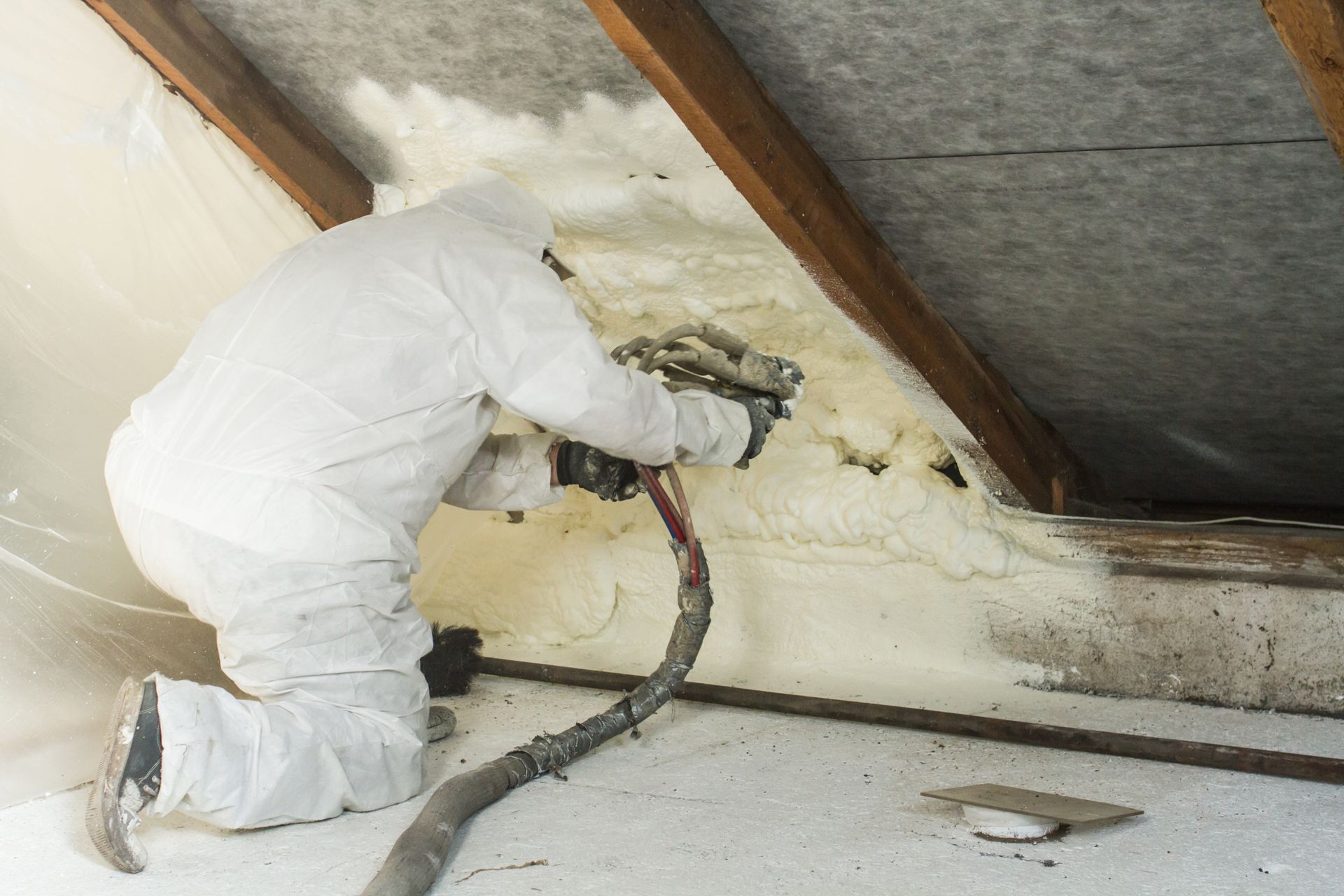 Person in protective suit spraying foam insulation in an attic