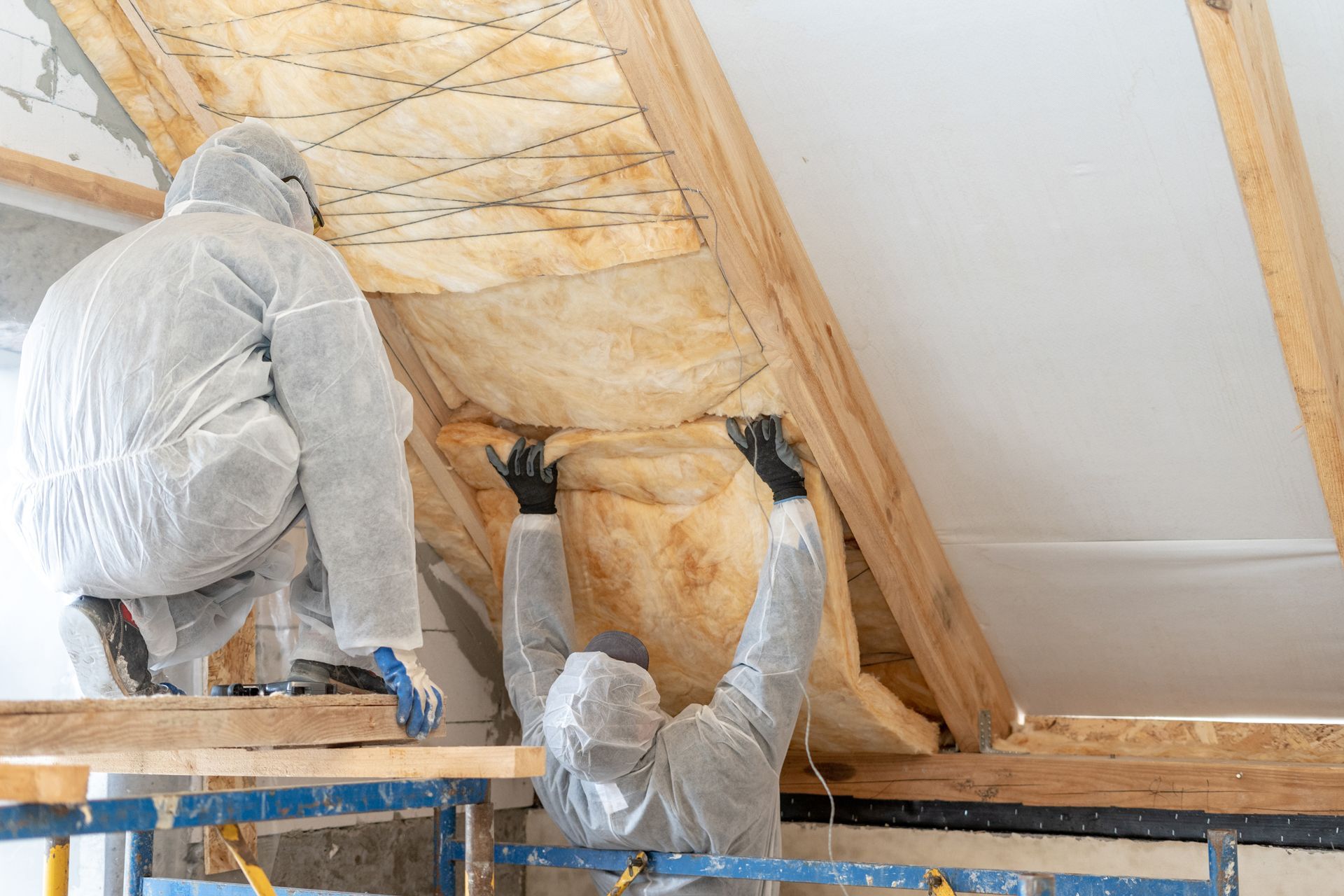 Two workers in protective suits installing insulation in an attic