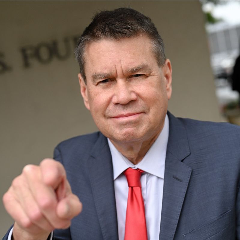 A man in a suit and tie is pointing at the camera