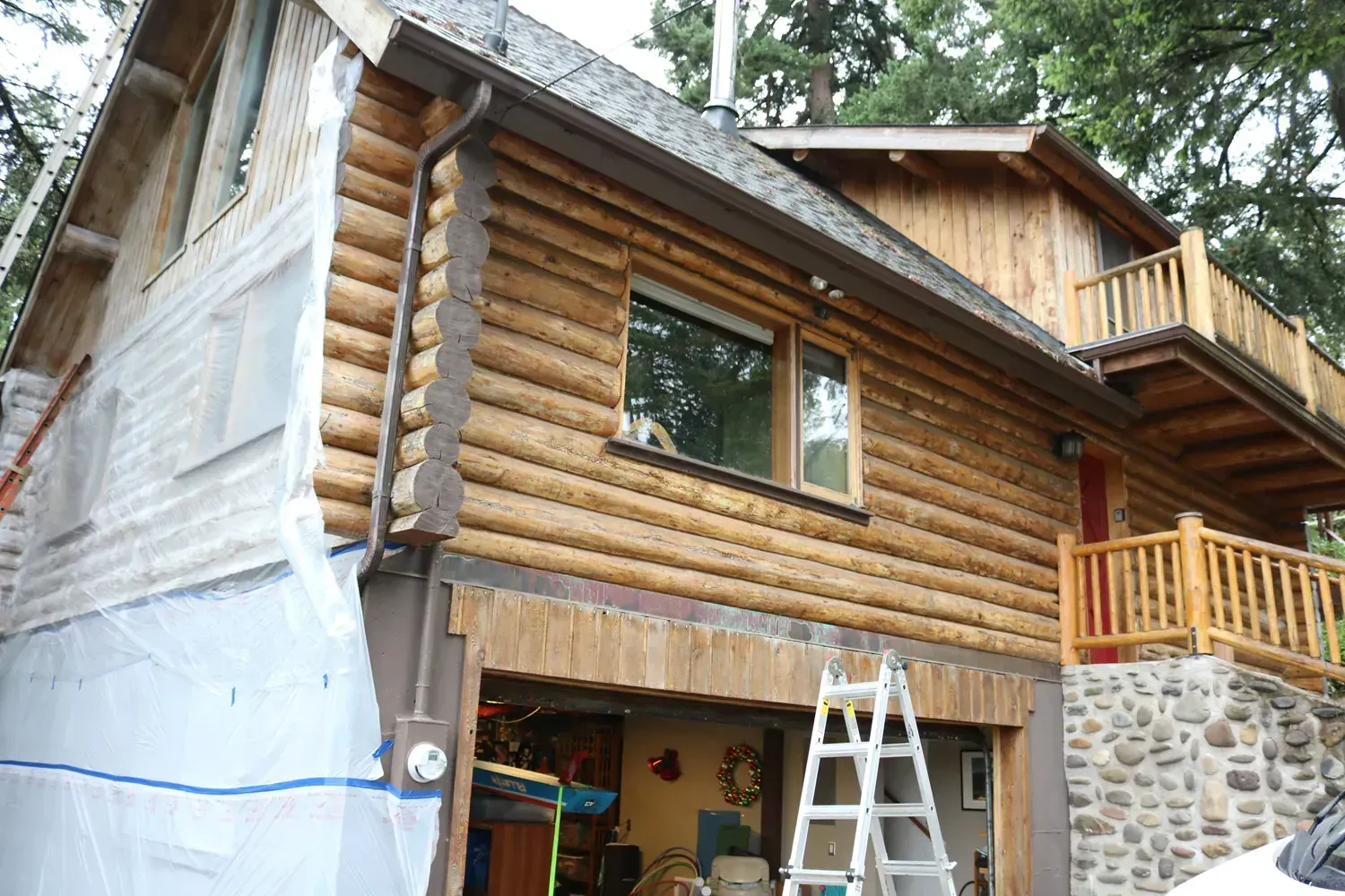A log cabin is being painted with a ladder in front of it.