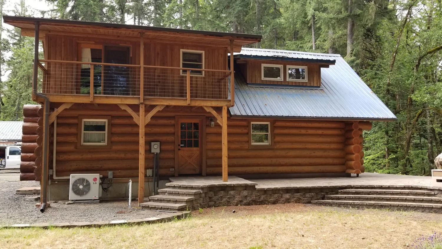 A log cabin with a balcony and stairs in the woods.