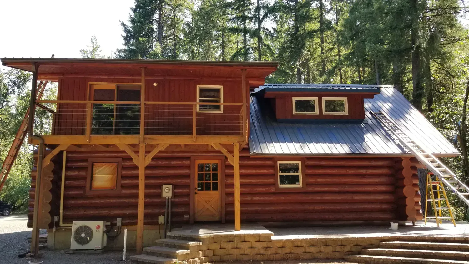 A large log cabin with a balcony and stairs in the woods.