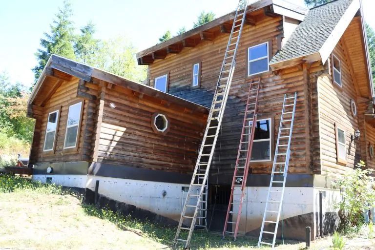 Two ladders are leaning against the side of a wooden house