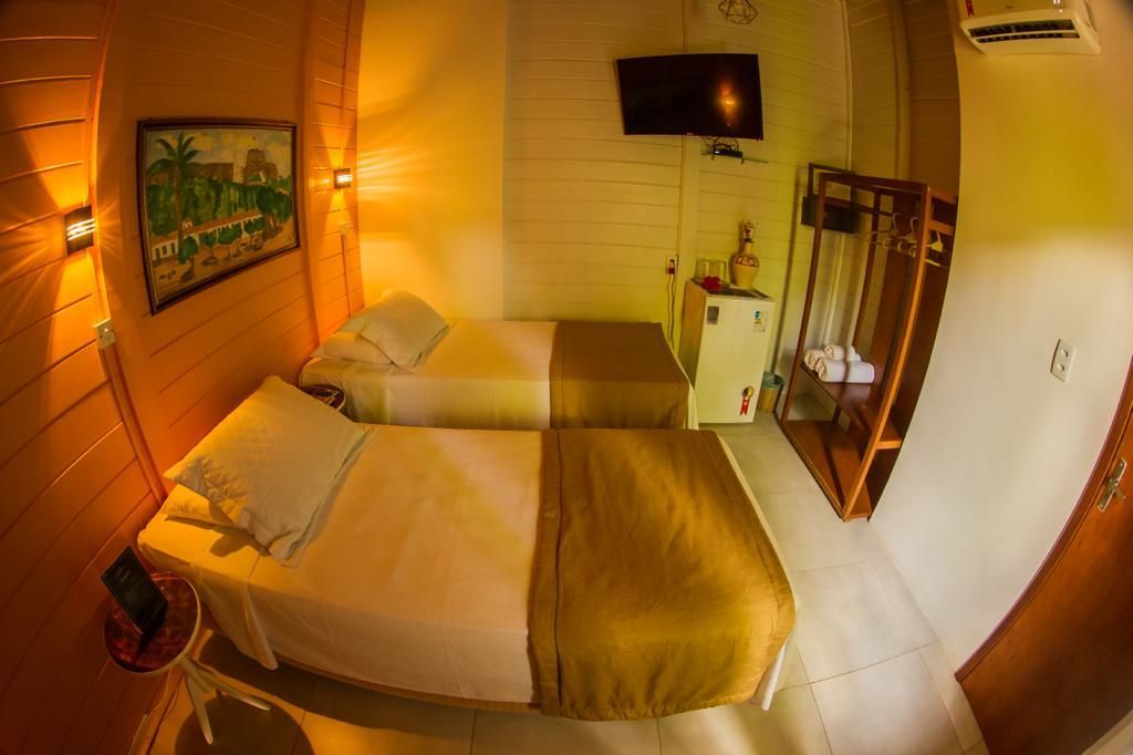 Quarto de hotel pequeno com duas camas de solteiro, TV pequena e guarda-roupa aberto.