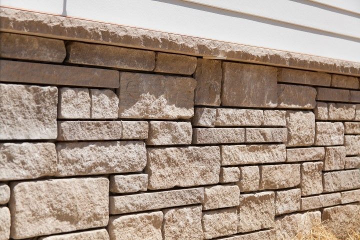 Stone retaining wall with tan and gray blocks beneath a white ledge