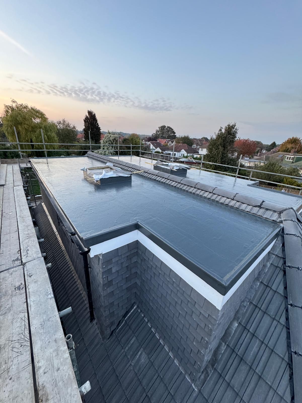 Person wearing red gloves unrolling black roofing material on plywood.