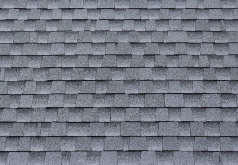 Roofer repairing a partially dismantled flat roof with exposed wooden beams, a skylight, and adjacent buildings.
