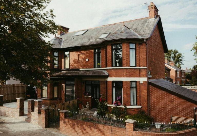 Roofer nailing shingles onto a roof under a bright blue sky.