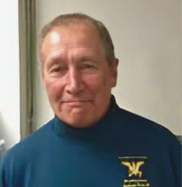 A man is wearing a blue turtleneck sweater with a yellow logo on the front.