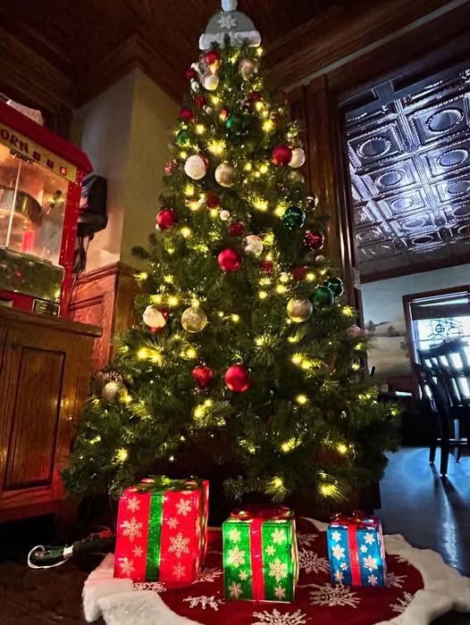 Christmas tree decorated with ornaments and lights, presents at the base, in a room with antique decor.