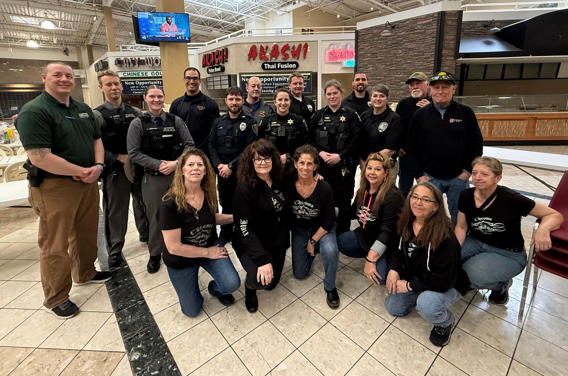 A group of police officers and volunteers posing for a photo in a shopping mall food court.