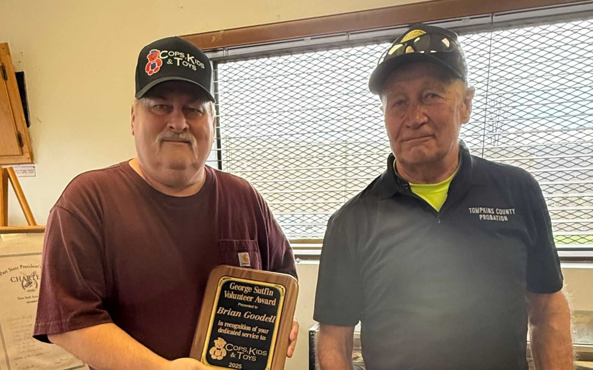 Two men standing, one holding an award plaque.