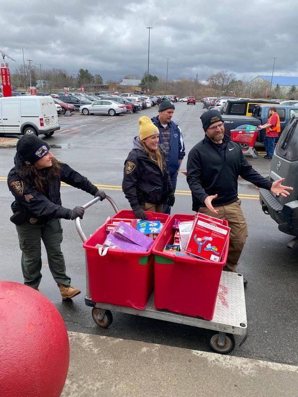 People loading donations into a vehicle, red bins on a cart outside a store, under an overcast sky.