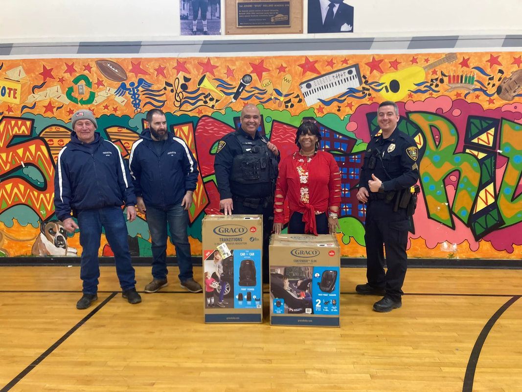 A group of people standing on a basketball court next to two car seat boxes.