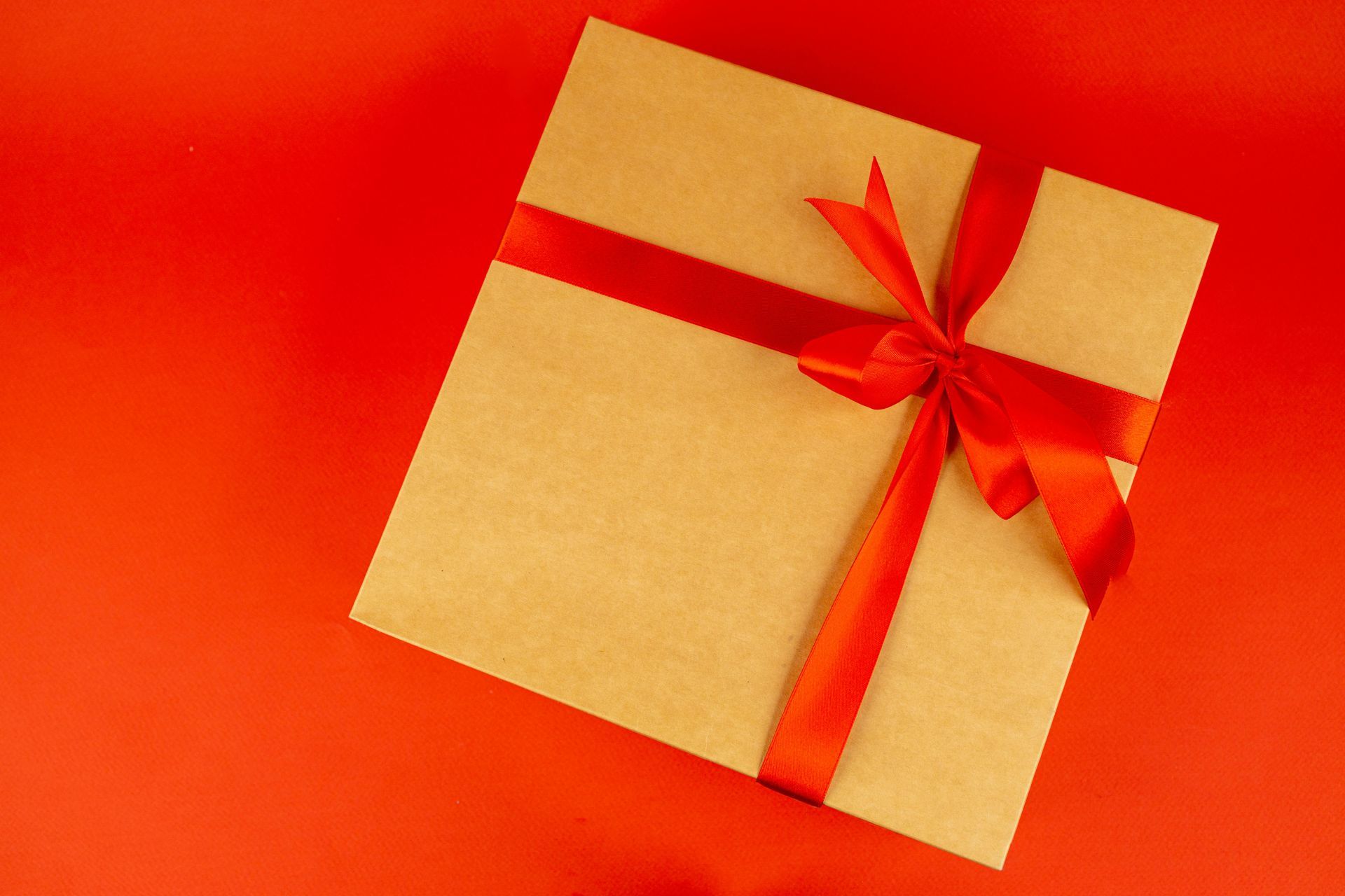 A gift box with a red ribbon and bow on a red background.