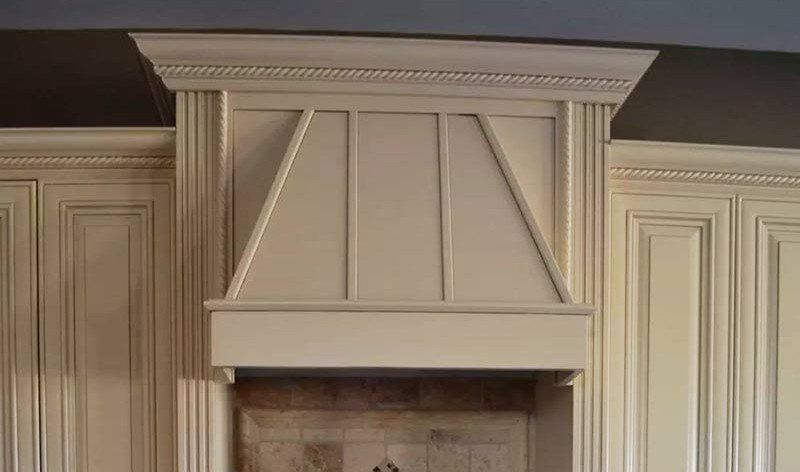 White kitchen hood built into paneled cabinetry above a fireplace opening