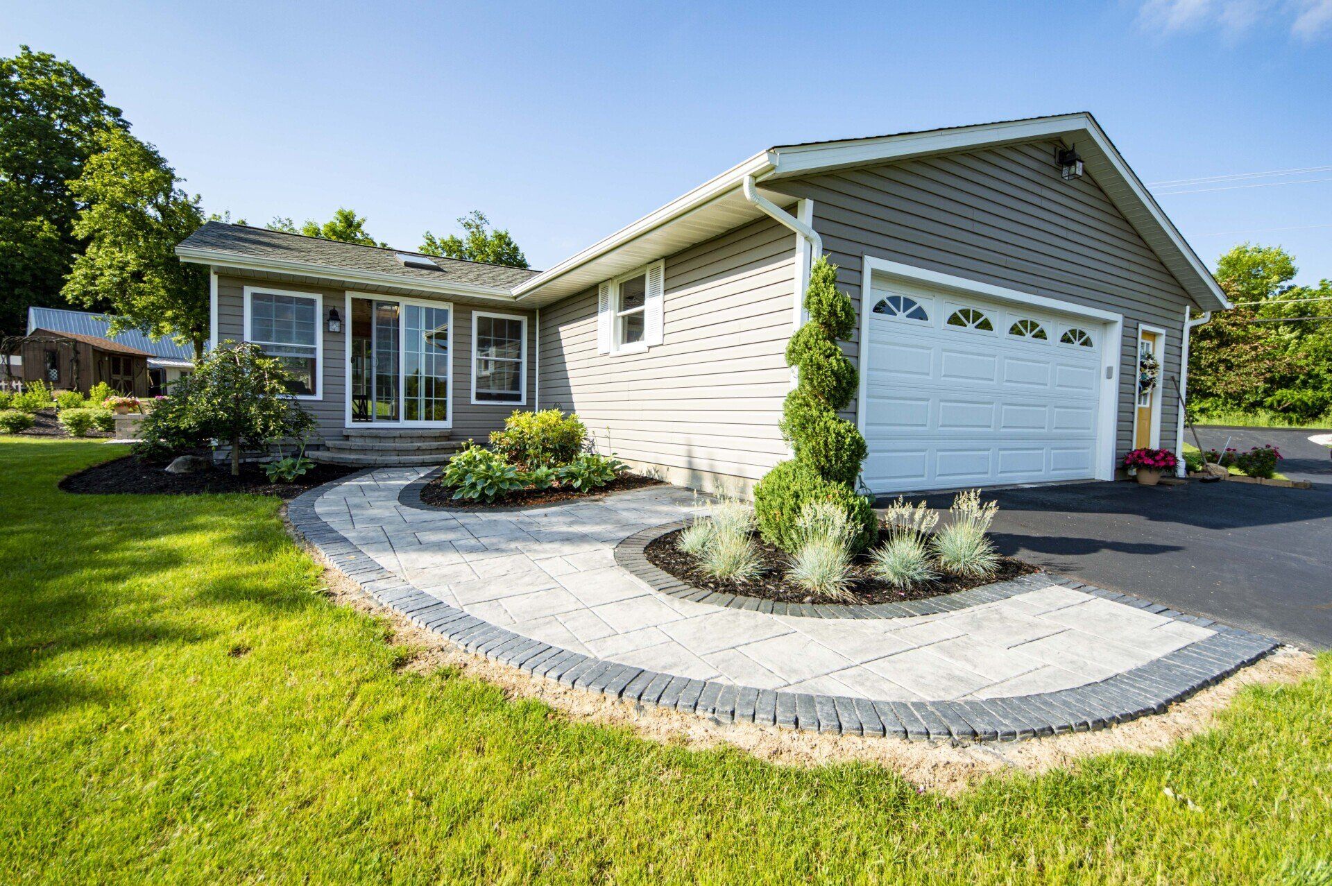 Gray house with stone walkway and landscaped yard. Garage door on right.