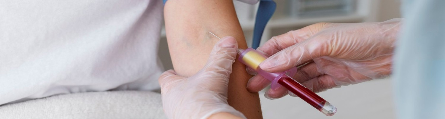 A person's arm being held while blood is drawn with a needle, by a gloved hand.