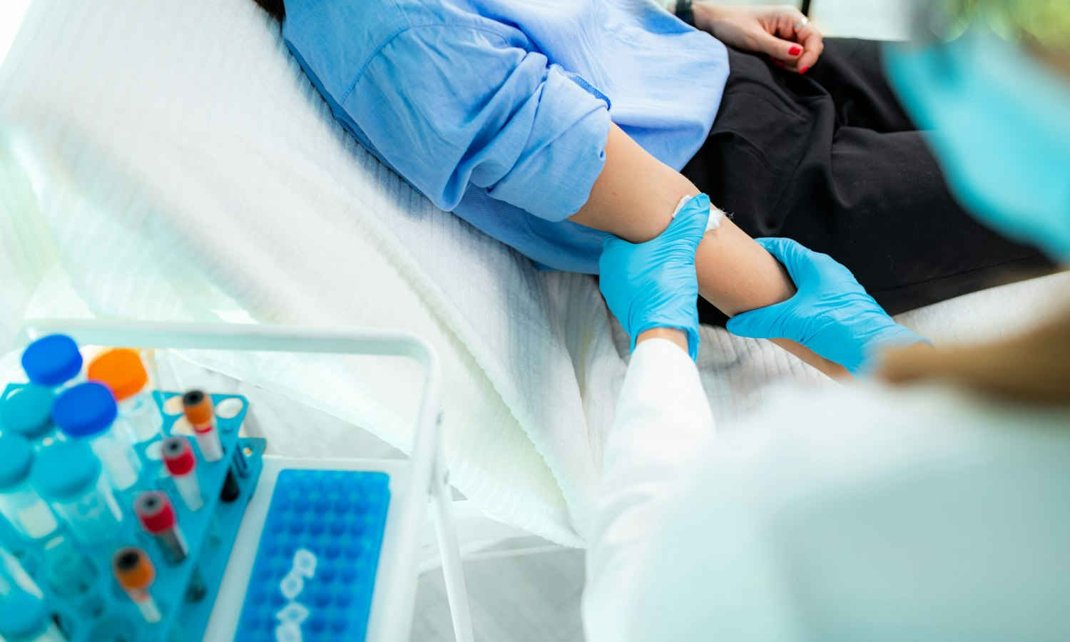 A person having blood drawn from their arm in a medical setting, with vials in the foreground.