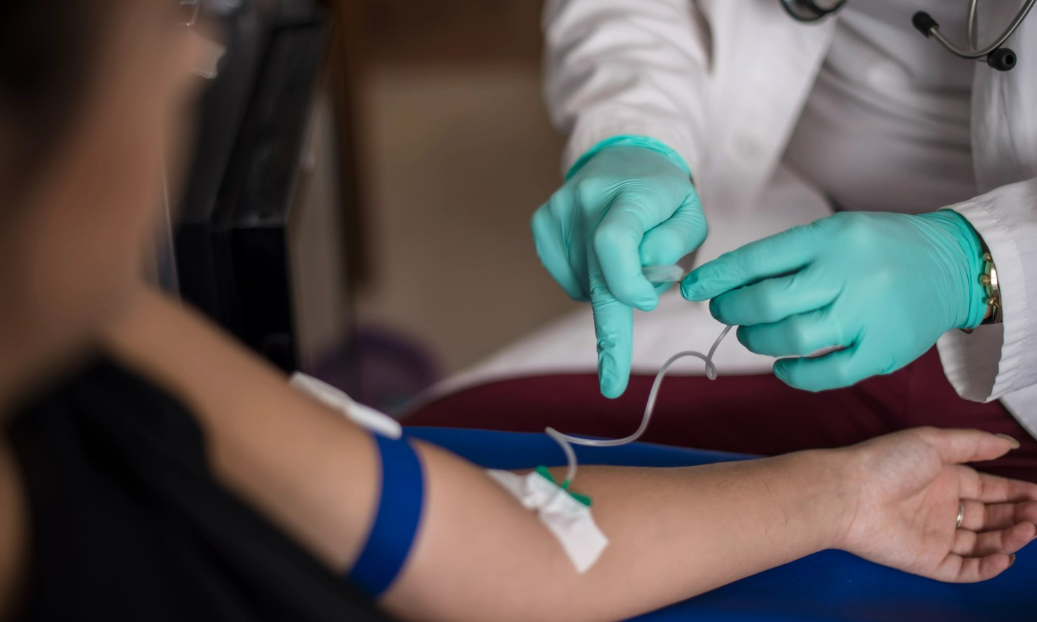 Person receiving blood transfusion. A doctor in gloves prepares the IV line.