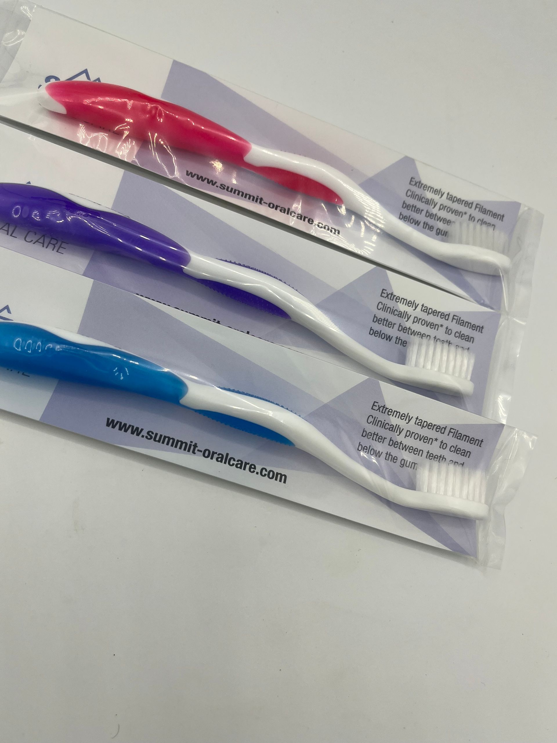 Three different colored toothbrushes are wrapped in plastic