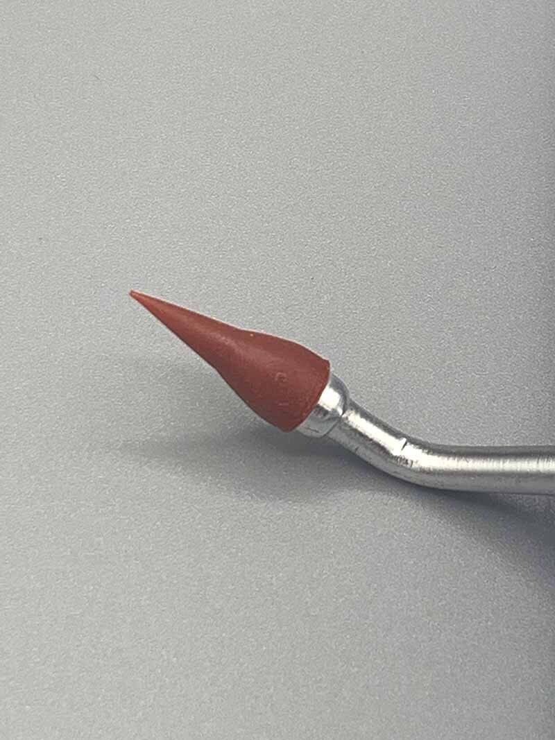 A close up of a needle with a red tip on a gray surface.