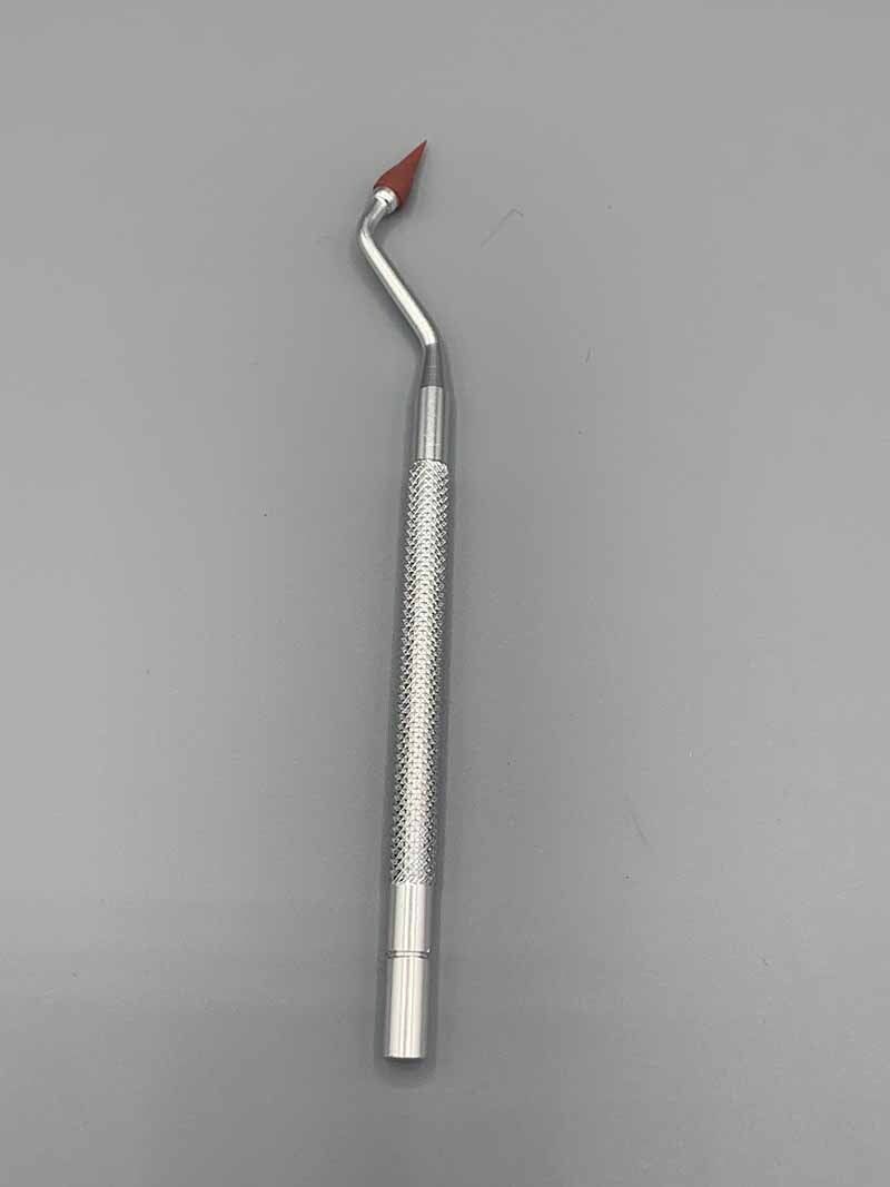 A dental instrument with a red tip is sitting on a gray surface.