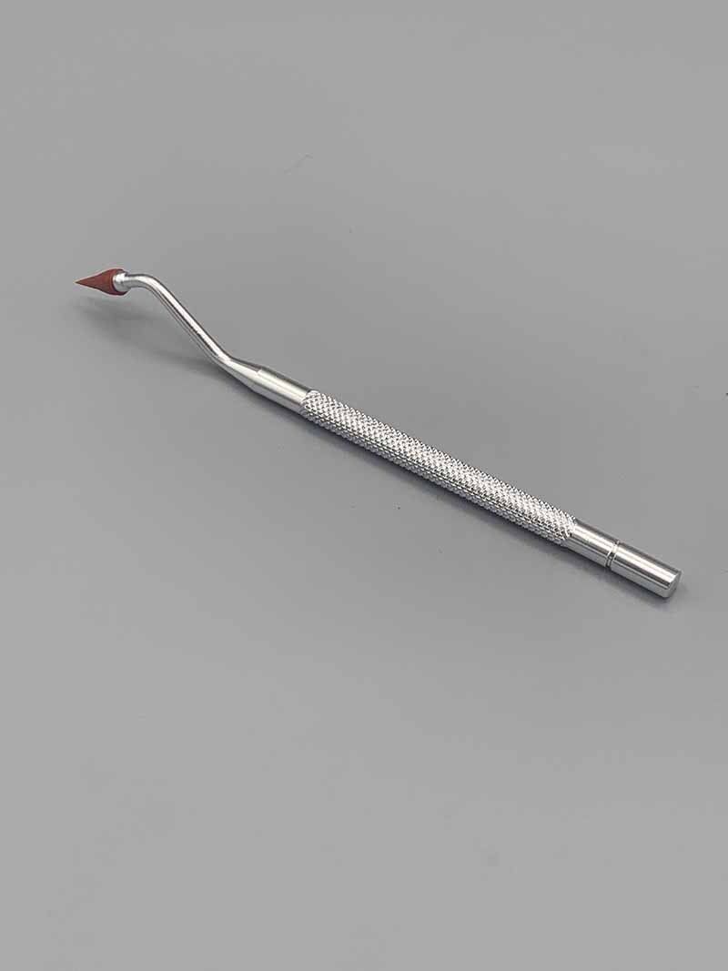 A dental tool with a red tip is sitting on a gray surface.