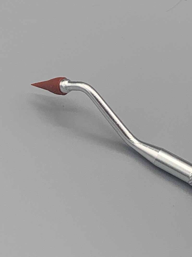 A close up of a dental instrument with a red tip on a gray surface.