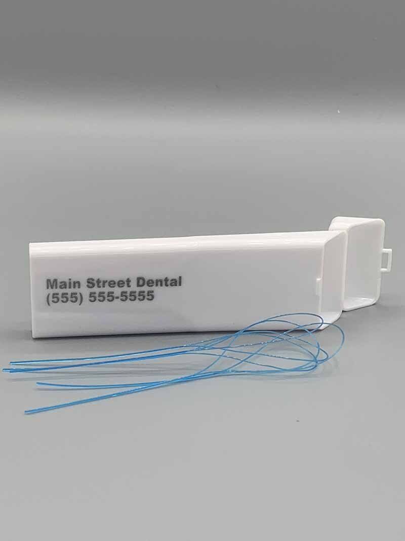 A white dental floss holder with blue floss on a gray surface.