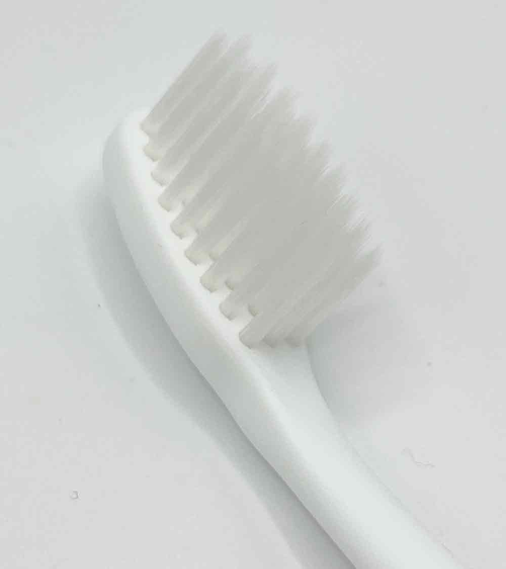 A close up of a white toothbrush on a white surface.