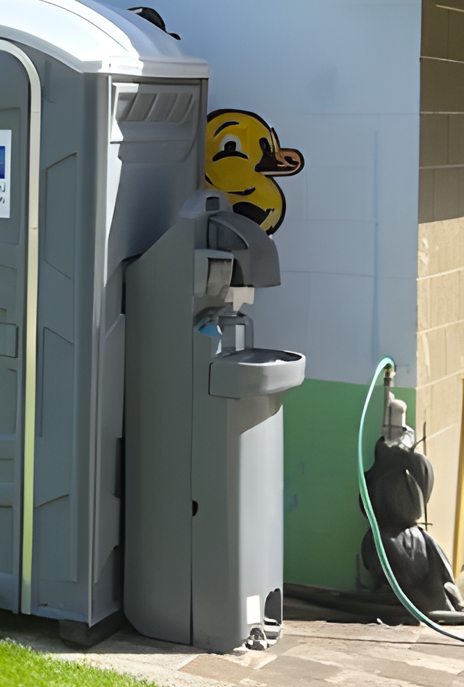 Portable toilet beside a house, with a yellow hard hat and utility equipment nearby.