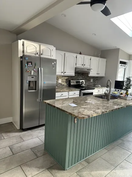 Bright kitchen with stainless steel fridge, white cabinets, and a teal island with granite countertop.