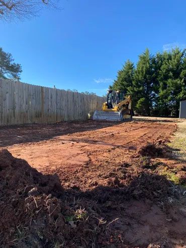 A bulldozer is moving dirt in a yard next to a wooden fence.